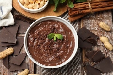 Tasty chocolate pudding in bowl and ingredients on wooden table, flat lay
