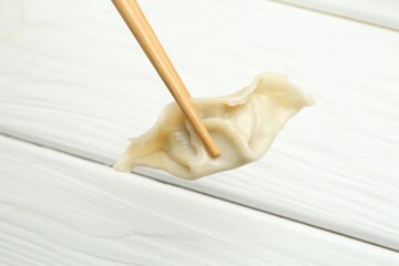 Chopsticks with tasty boiled gyoza dumpling over white wooden table, closeup