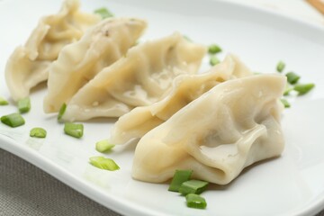 Tasty boiled gyoza (dumplings) with green onion on white table, closeup