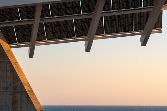 Solar panel pergola at sunrise, with warm tones reflecting off the metallic surfaces. A representation of green energy in urbanism.