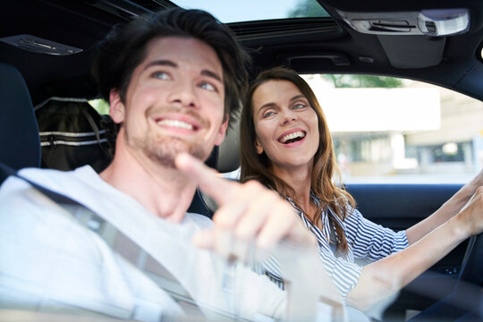 Happy couple in a car with woman driving and man pointing his finger - Powered by Adobe