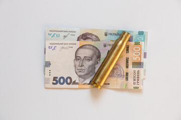 Ukrainian banknotes of 500 and 1000 denominations and a cartridge case lie on a white background, business and finance, money and weapons