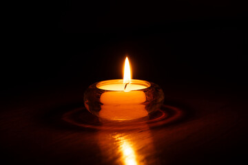 Burning candle in glass round candlestick on table at home in dark