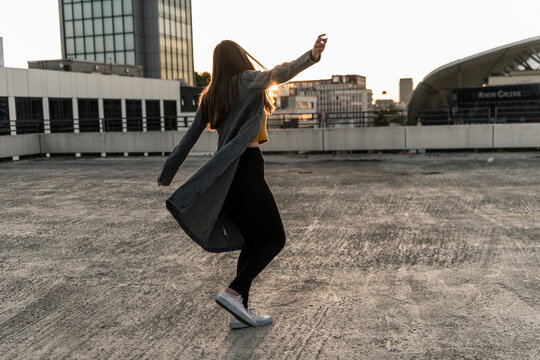 Cheerful young woman dancing on parking deck at sunset - Powered by Adobe