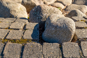 View of large stones among paved tiles in a sunny outdoor setting, showcasing natural elements and human-made surfaces