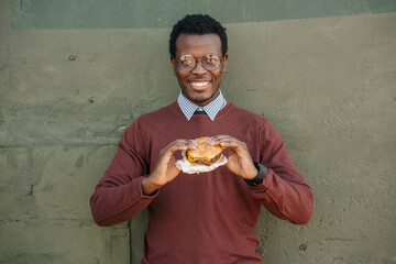 Young man eating cheeseburger, smiling