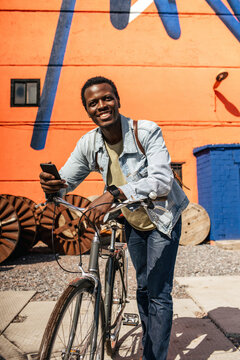 Relaxed young amn commuting in the city with hos bicycle, using smartphone