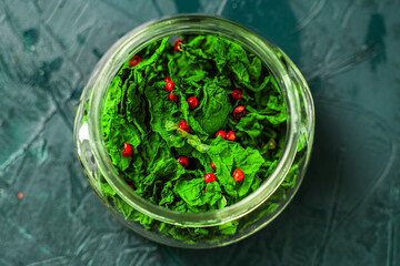Dried basil leaves and pink pepper in a glass jar on a malachite background. Close-up. View from above.