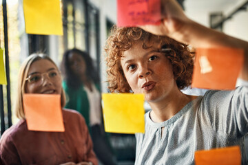 Colleagues writing on sticky notes at glass pane in office