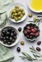 Bowls of black, green and kalamata olives with olive oil and olive branches on marble table