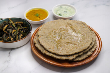 Roti and Sabzi. Indian vegetarian Thali includes bhindi fry, yellow daal tadka, cucumber raita, and jwari or jowar bhakri. Indian food is served in a plate or thali. Copy Space. healthy Veg Thali.