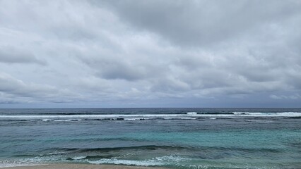 Tropical beach with turquoise waters and rolling waves, set against a dramatic cloudy sky