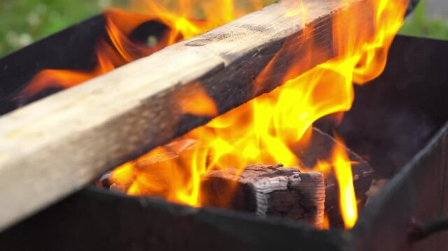 Fiery flames burning rapidly and charring a suspended piece of wood. Steady close up