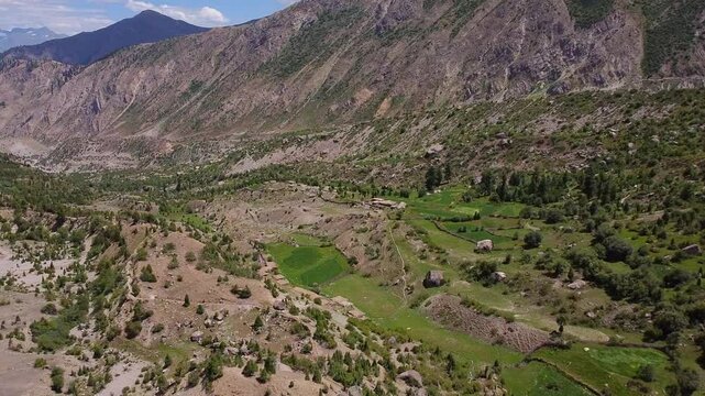 Aerial view capturing Rupal Valley's cultivated fields and trees with majestic Nanga Parbat rising in the background. Pull Back shot