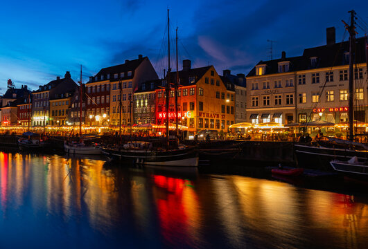 Kopenhagen, Dennmark - 1 June 2024: Night cityscape of embankment called Nyhavn in Dannish, yachts, colourful reflections of illuminations in the water, dramatic clouds in the skye.