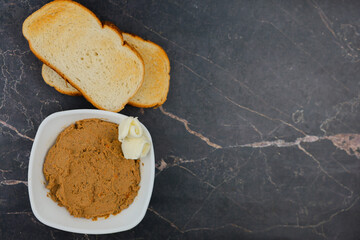 A white plate with liver pate and slices of butter, next to it are wheat bread toast on a dark background with space for text. The concept of snacking, wholesome and healthy food. High quality photo