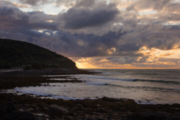 Dramatic sunset over rocky shore of Pacific Ocean near Raglan, New Zealand