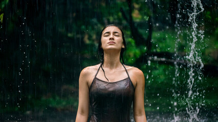 Obraz premium Serene Woman Standing by Waterfall Amid Lush Greenery Enjoying Nature's Serenity