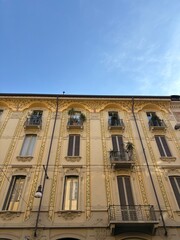 Charming vintage architecture in the city of Milan, Italy, with ornate patterns and decorative elements on buildings. The building is yellow and has green details. Blue sky background.