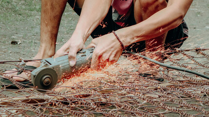 A person is using an angle grinder to cut through a metal spring mattress, with sparks flying from the cutting process