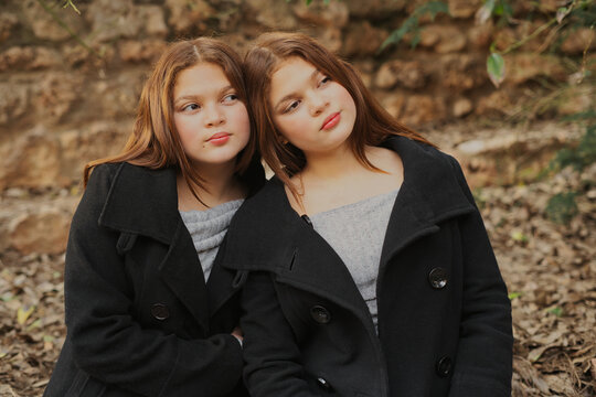 Twin sisters wearing black coats sitting in autumnal park