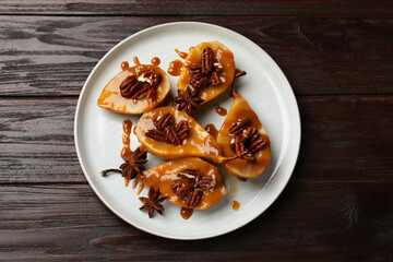 Delicious pears with caramel sauce, pecan nuts and anise stars on wooden table, top view