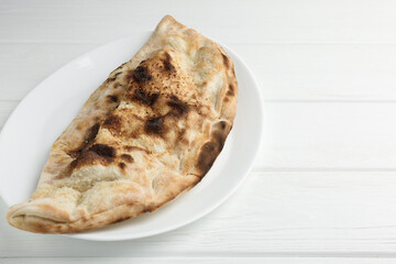 Plate with tasty calzone on white wooden table, closeup. Space for text