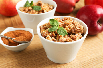 Delicious apple crisp with mint in bowls, cinnamon and fresh fruits on wooden table, closeup