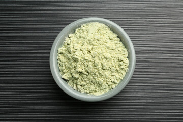 Wasabi powder in bowl on black textured table, top view