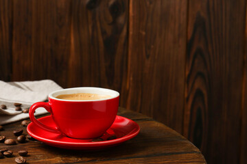 Red cup with coffee and roasted beans on wooden table, space for text
