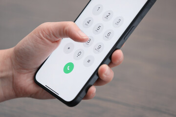 Woman dialing number on smartphone against blurred background, closeup