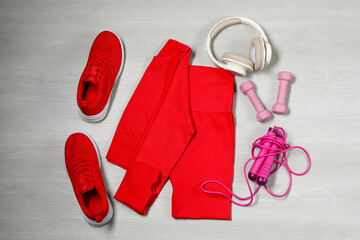 Stylish sportswear, red sneakers, dumbbells, skipping rope and headphones on wooden background, flat lay