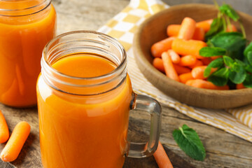 Fresh carrot juice in mason jars, vegetables and mint on wooden table, closeup