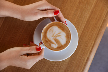 Woman with cup of aromatic coffee at wooden table in cafe, top view