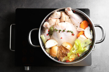 Whole fresh turkey, cut onion, carrot, celery, spices in pot and stove on grey table, top view