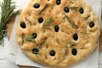 Delicious focaccia bread with olives and rosemary on white wooden table, top view
