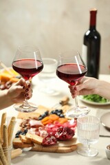Women clinking glasses of wine during dinner at table indoors, closeup