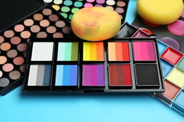 Bright face paints and sponges on light blue background, closeup