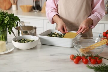 Woman making spinach lasagna at marble table indoors, closeup