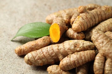 Pile of tumeric rhizomes with leaf on grey table, closeup