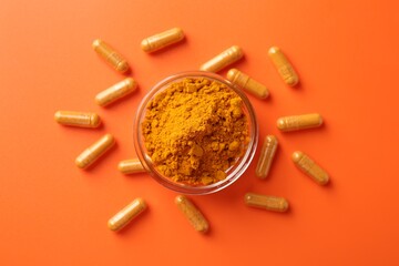 Turmeric capsules and powder on orange background, flat lay