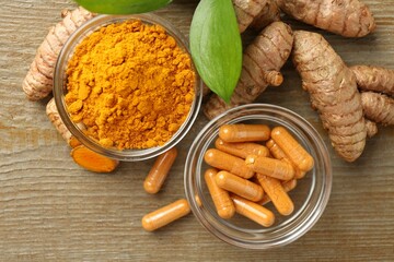 Turmeric capsules, powder, roots and green leaves on wooden table, flat lay