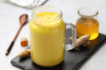 Delicious turmeric latte with honey and rhizomes on grey table, closeup