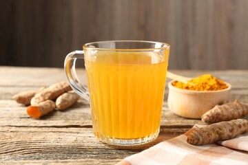 Aromatic turmeric tea in glass mug, roots and powder on wooden table, closeup