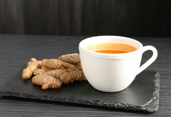 Aromatic turmeric tea and rhizomes on black table, closeup