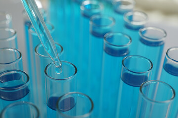 Dripping liquid into test tubes on light background, closeup