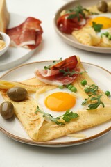 Delicious crepes with eggs and bacon served on white table, closeup