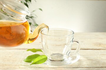 Pouring freshly brewed tea from teapot into glass cup on wooden table, closeup