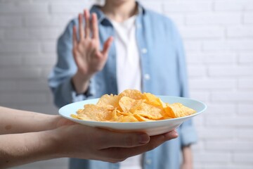 Woman refusing chips near white brick wall, selective focus. Food allergy concept