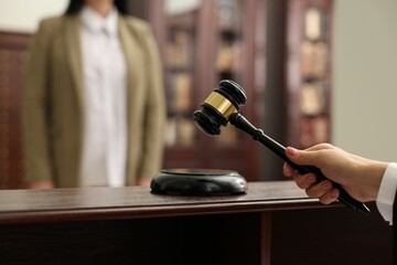 Judge striking gavel at wooden table in courtroom, closeup